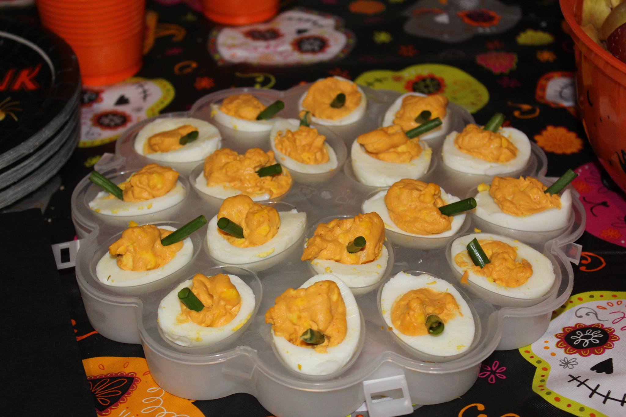 platter of deviled eggs filled with orange filling and topped with green onion pieces to look like pumpkins