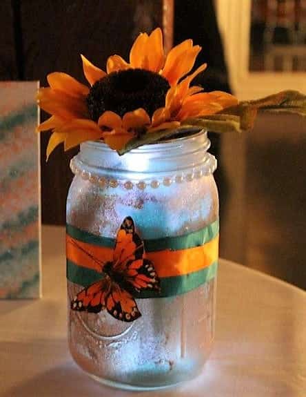 glittery mason jar with a sunflower top wrapped in orange and teal ribbon