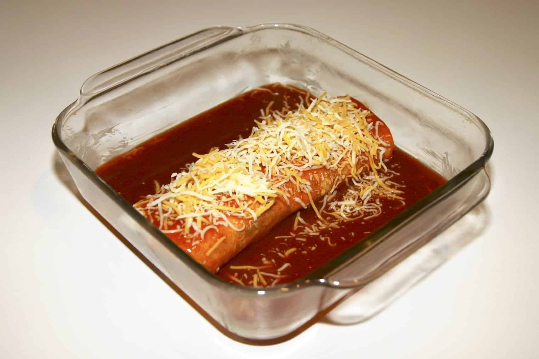 rolled tortilla in red enchilada sauce with shredded yellow and white cheese on top
