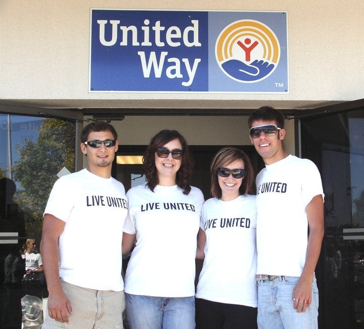 two brunette girls standing with a brunette man on either side, all wearing sunglasses and white shirts that say Live United, under United Way Sign