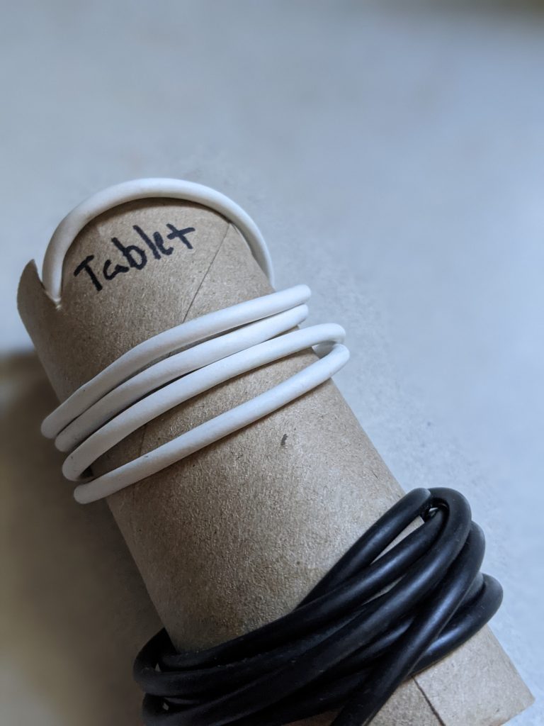 Toilet paper tube with electronics cables wrapped around, labeled "tablet" and "cell"